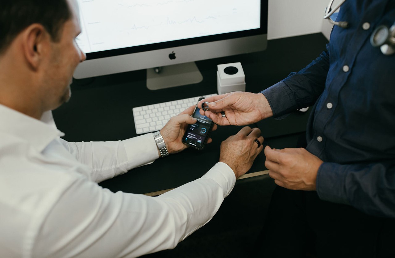 A clinician showing an Edison member a health-tracking ring and a phone dashboard of their health data